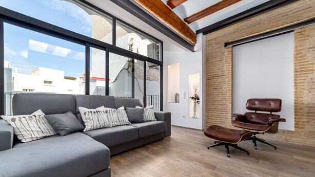 A modern living room with a grey sectional sofa, a brown leather chair, and a large window offering a view of buildings. - CENTER-Luxurious 1BR, 1BA-Terrace, WI-FI, A/C (Valencia)