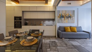 Een moderne keuken met inbouwapparatuur, een eethoek met een glazen tafel, en een grijze bank met gele kussens.