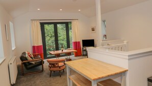 Ein Essbereich mit einem Holztisch, Bänken, einem Fernseher und Blick auf Grün durch große Fenster.
