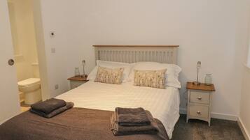 A bedroom with a bed, two bedside tables, a nightstand, a wooden headboard, and a door leading to a bathroom.