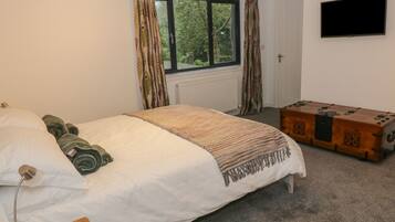 A bedroom with a bed, a bedside lamp, a wooden chest, and a window with curtains.