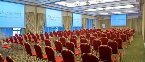 A conference room with rows of red chairs, a carpeted floor, and large screens displaying 'Klub Sosnowy'.