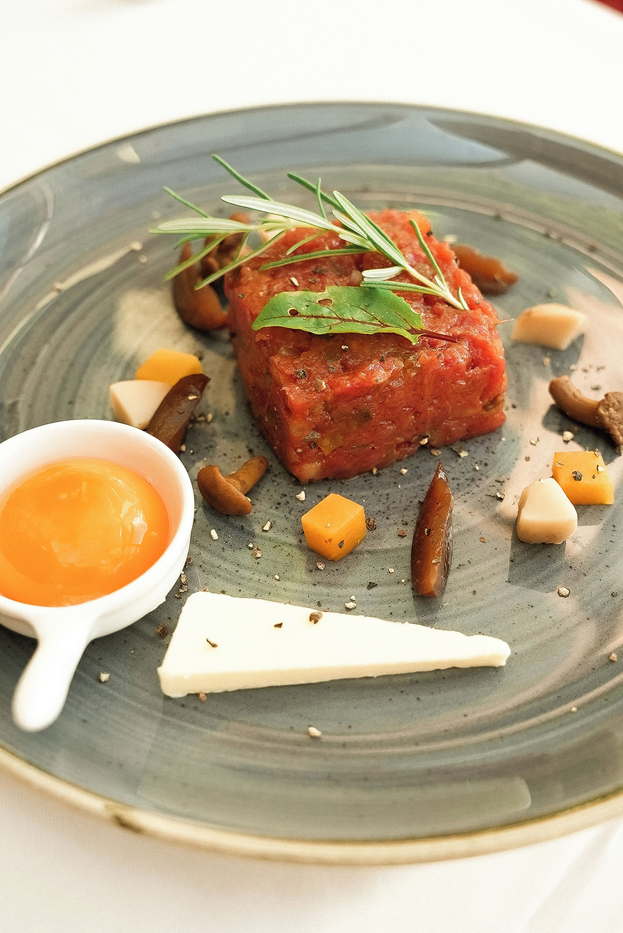 A plate with a dish of food, a small bowl of sauce, and some nuts.