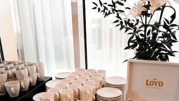 A table with stacks of beige cups, plates, and a basket of silverware.