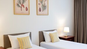 Habitación de hotel con dos camas, cada una con una almohada y una mesita de noche con lámpara.
