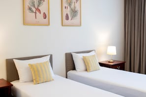 A hotel room with two beds, each with a pillow and a nightstand with a lamp.