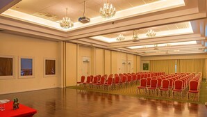 Un salón de conferencias con hileras de sillas rojas, un proyector y candelabros.