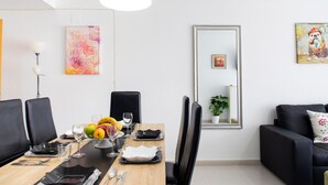 Ein Essbereich mit einem Holztisch, gedeckt für vier Personen, schwarzen Stühlen und einer Obstschale. An den Wänden befinden sich ein großer Spiegel und Kunstwerke.