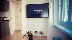 Un salon moderne avec un téléviseur à écran plat affichant le logo de Prime Video, une petite table ronde avec deux tasses, une plante en pot et une télécommande posée sur un banc.