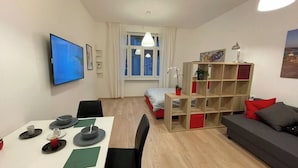 Un salon moderne doté d’un téléviseur à écran plat, d’un coin repas avec une table dressée pour deux personnes, d’un canapé et d’une bibliothèque.