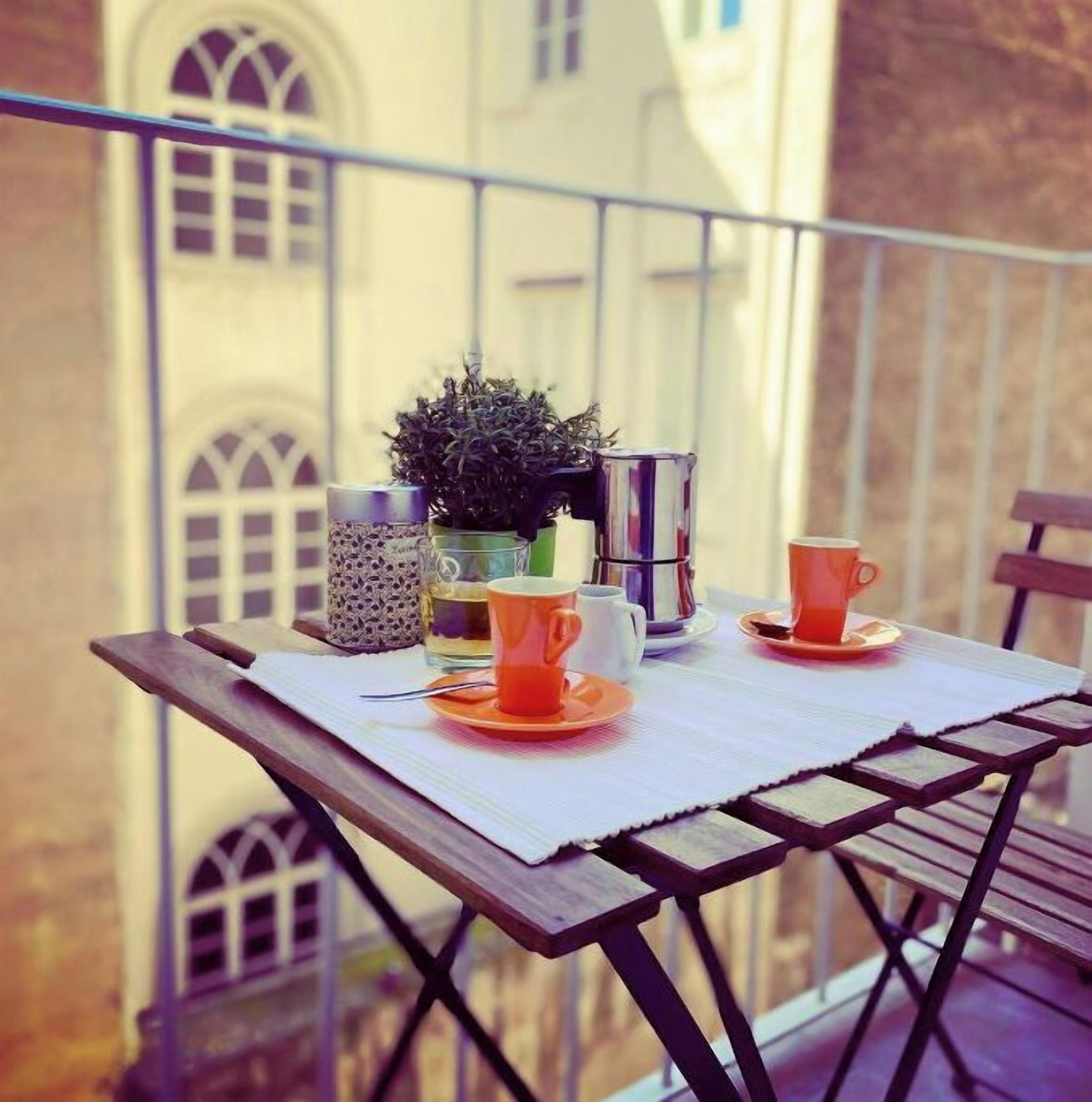 A balcony table with a potted plant, two orange cups, and a glass.