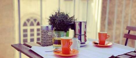 A balcony table with a potted plant, two orange cups, and a glass.