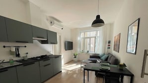 Une cuisine moderne avec des meubles gris, un coin repas comprenant une table et des chaises, et une grande fenêtre qui laisse entrer la lumière naturelle.