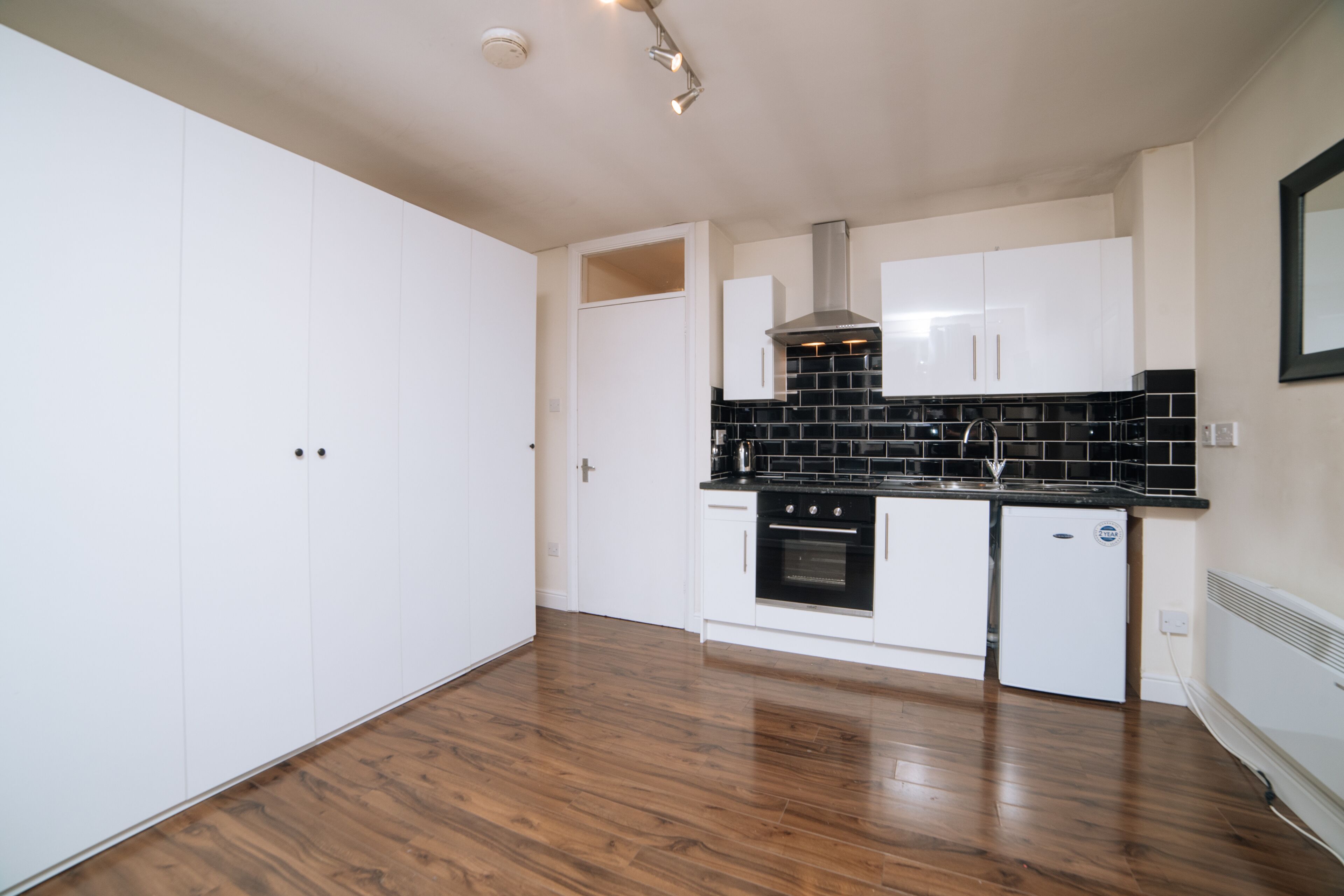 A modern kitchen with white cabinets, a black tiled backsplash, and a stainless steel range hood.