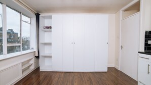 Huoneessa on suuri vaatekaappi, ikkunasta avautuu näkymä rakennuksiin ja lattia on tehty puusta.