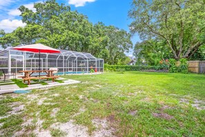 Enjoy a sheltered outdoor space with a picnic table and small pool amidst a lush lawn and vibrant plants.