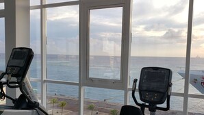 Une salle de sport équipée de matériel d’exercice et offrant une vue sur la mer grâce à de grandes fenêtres.