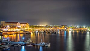 Un port de plaisance la nuit, avec des bateaux amarrés, une promenade en bord de mer et des bâtiments dont les enseignes sont illuminées.