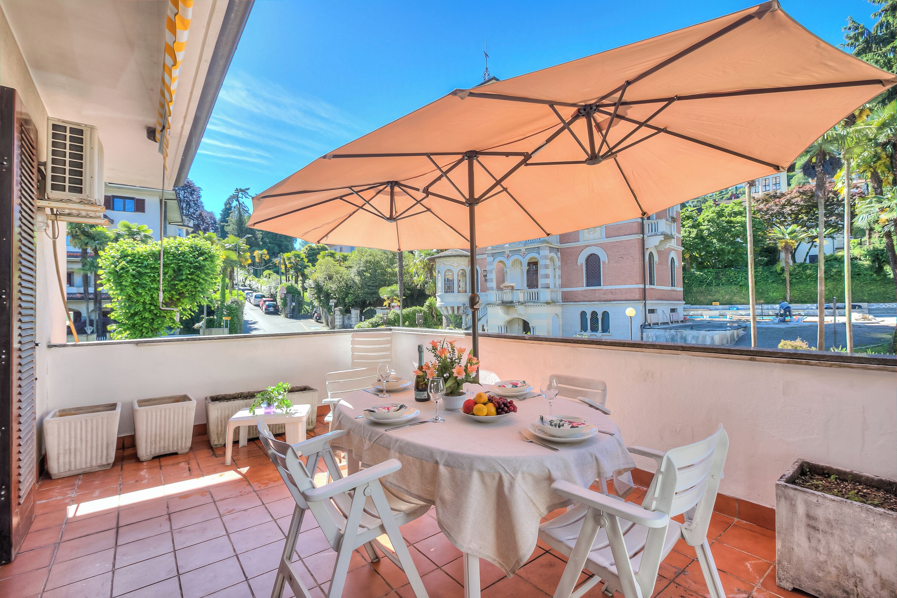 Eine Terrasse mit Esstisch, großem Sonnenschirm und Blick auf ein historisches Gebäude.