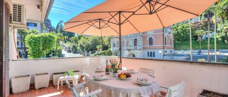 Eine Terrasse mit Esstisch, großem Sonnenschirm und Blick auf ein historisches Gebäude.