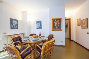 A dining area with wicker chairs, a round table, and wall art including a floral painting. - Appartamento Gaya Stresa Center (Stresa)
