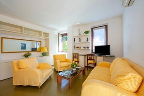 Uma sala de estar com sofás de listras amarelas, uma mesa de centro com flores, uma televisão e uma estante com objetos decorativos.
