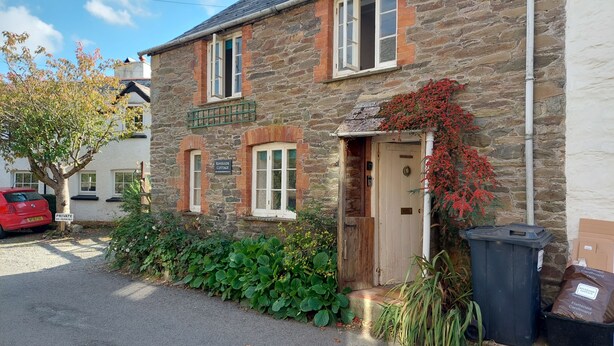 Une petite maison en pierre avec une porte en bois, une enseigne indiquant « Riverside Cottage » et un panneau « Stationnement interdit ».