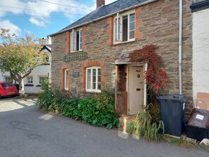 A stone cottage with a wooden door, a sign indicating 'Riverside Cottage', and a 'No Parking' sign. - Riverside Cottage Brendon (Lynton)