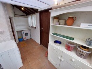 A laundry area with a washing machine, drying rack, and shelves with storage containers. - Riverside Cottage Brendon (Lynton)