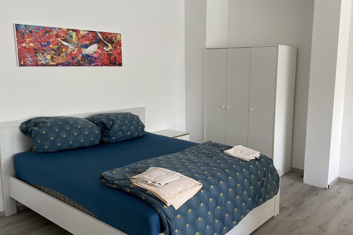 A bedroom with a bed, pillows, a wardrobe, and a painting on the wall.