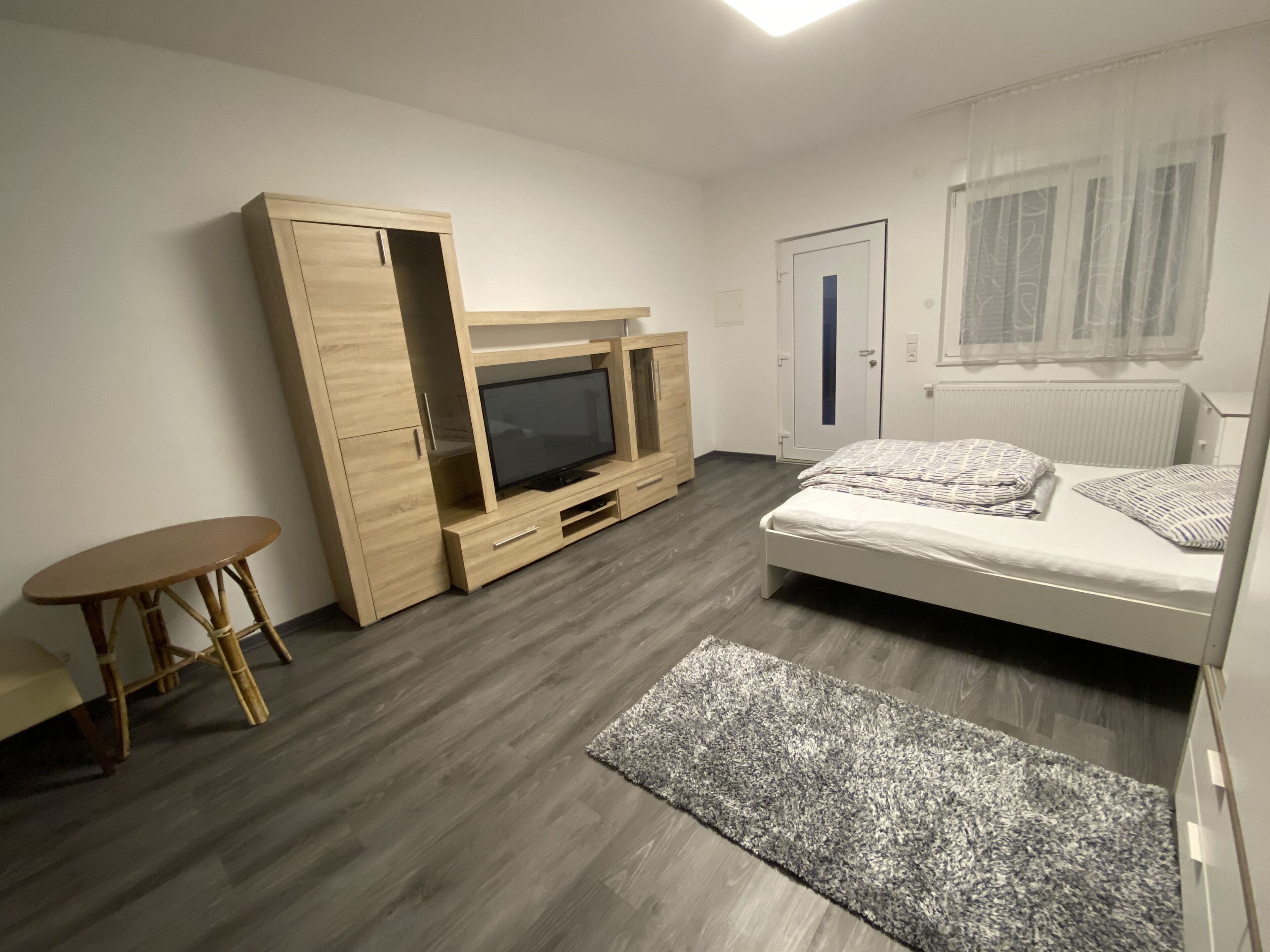 Ein modernes Schlafzimmer mit einem Bett, einem Fernseher auf einem Holzständer, einem kleinen Tisch und einem Kleiderschrank.