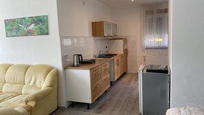 A compact kitchen with a microwave, kettle, and a small sink. There is a beige sofa and a refrigerator in the room. - Pension Neon (Mannheim)