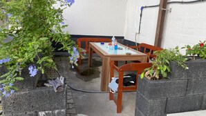 A small outdoor dining area with a wooden table and chairs, surrounded by plants and a stone wall. - Pension Neon (Mannheim)