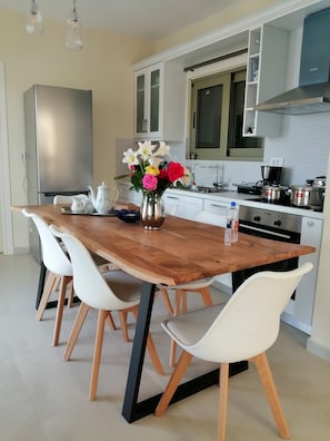 Una cocina moderna con armarios blancos, un refrigerador de acero inoxidable, una mesa de comedor de madera con sillas blancas y un florero con flores.