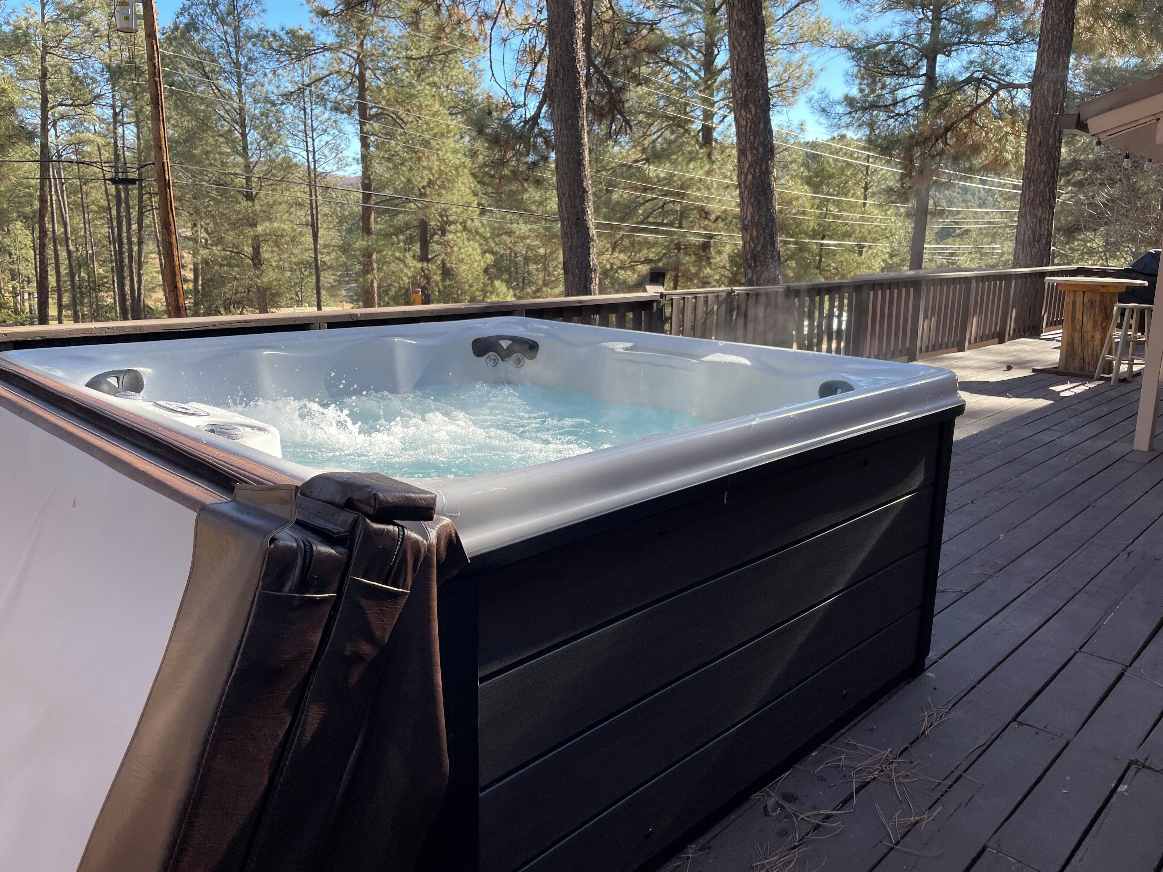 Un jacuzzi en una terraza de madera con un bosque de fondo.