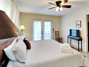 A bedroom with a bed, a ceiling fan, a television on a stand, a chair, and a door with a window. - Elks Landing by Ruidoso Vacation Rentals (Ruidoso)