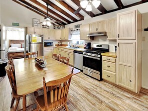 A kitchen with wooden cabinets, a stove, and a dining area with a wooden table and chairs. - Elks Landing by Ruidoso Vacation Rentals (Ruidoso)