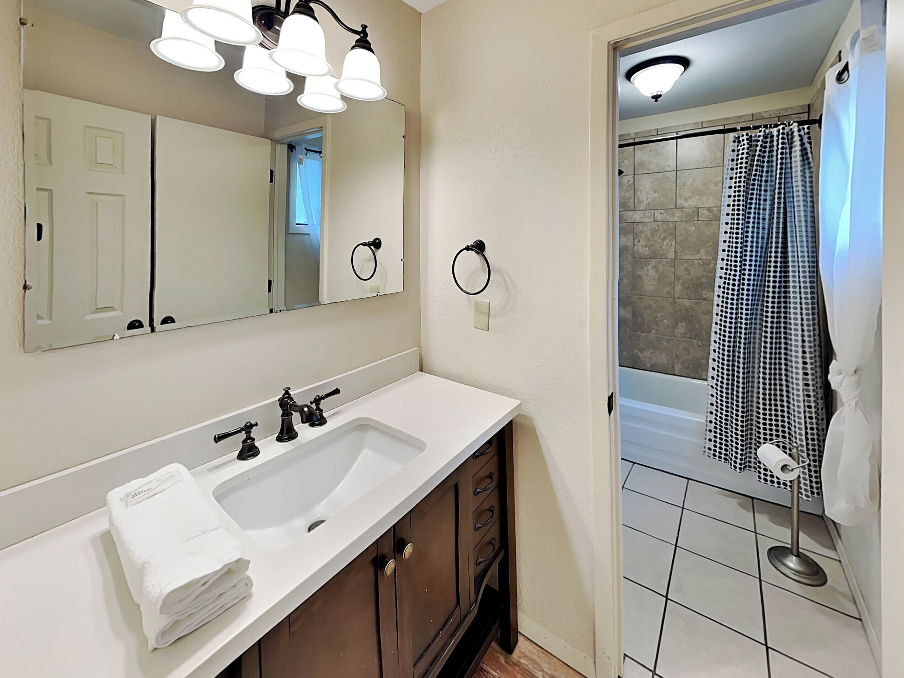 A bathroom with a white sink, dark wooden cabinets, a large mirror, and a shower with a black and white patterned curtain.