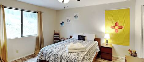 A bedroom with a bed, a ceiling fan, a nightstand, a lamp, and a window with curtains.