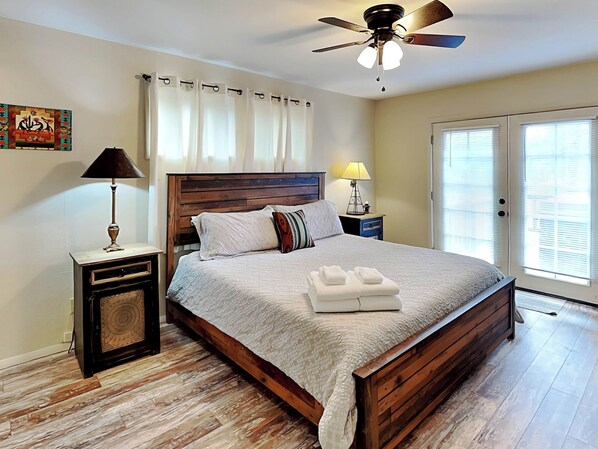 A bedroom with a wooden bed, two bedside tables with lamps, a ceiling fan, and a window with blinds. - Elks Landing by Ruidoso Vacation Rentals (Ruidoso)