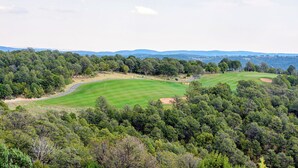 Un parcours de golf entouré d’une forêt dense, avec des collines ondoyantes en arrière-plan.