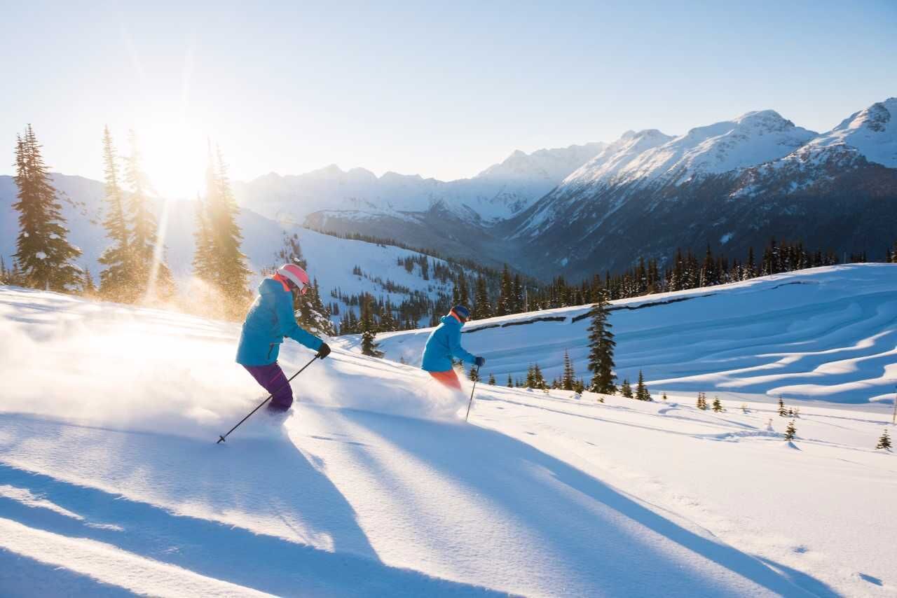 A snowy mountain landscape with two skiers.