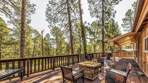Une terrasse en bois, meublée pour l’extérieur, avec un foyer et une vue sur de grands arbres.