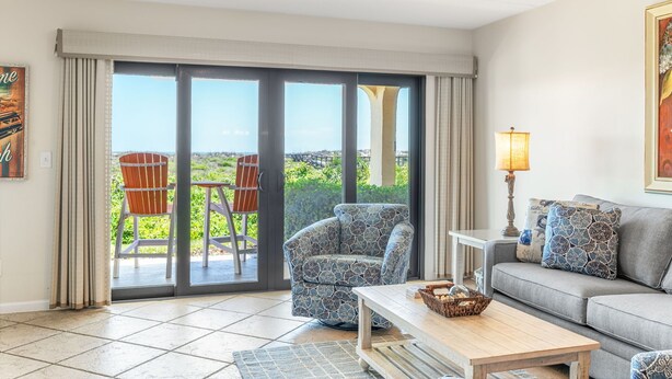 A living room with a sofa, armchair, and table, a balcony with chairs, and a large window with a view. - NEW LISTING!!! DIRECT OCEAN FRONT 1st FLOOR SEA PLACE CONDO!!! 2bd/2 bath (St. Augustine)