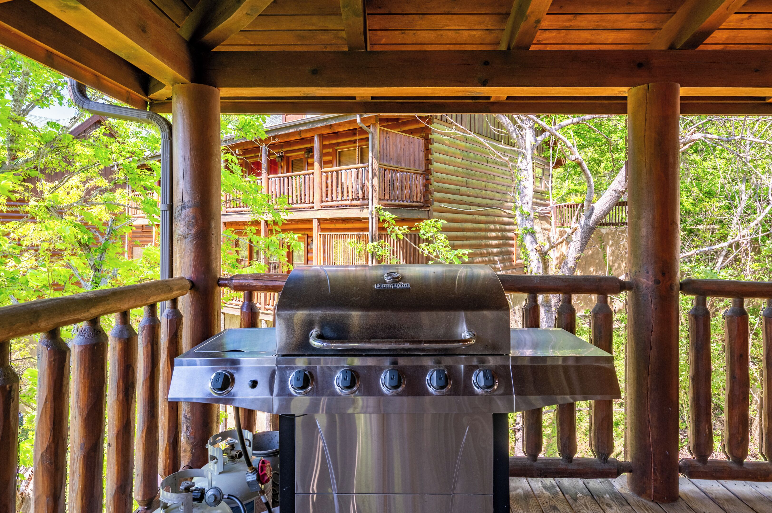 A wooden deck with a barbecue grill, a wooden fence, and a wooden building with a balcony in the background.