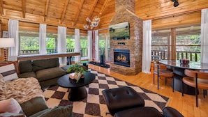 A spacious living area with a fireplace, wooden ceiling, and large windows. - Timberwolf Vista w HotTub Pool View (Sevierville)