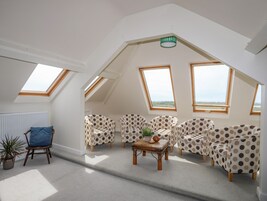 Un espacioso dormitorio tipo loft con techo inclinado, ventanas amplias y una zona de estar acogedora con muebles a lunares.