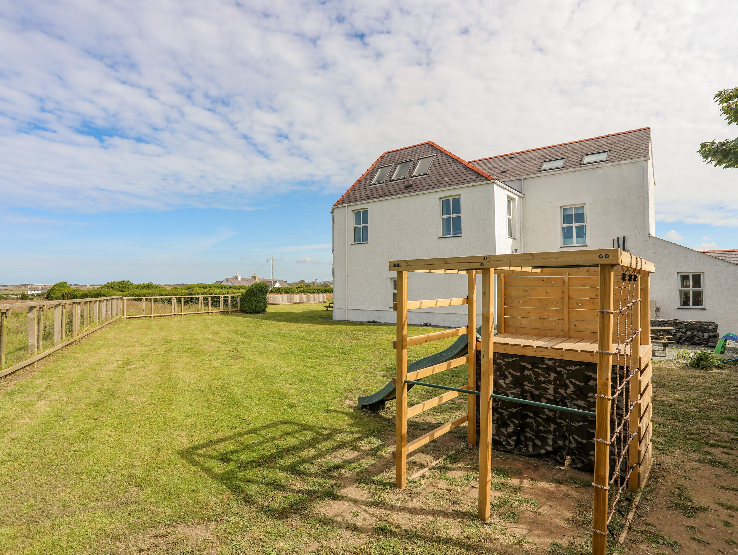 A white house with a red roof, a wooden play structure, and a grassy yard.