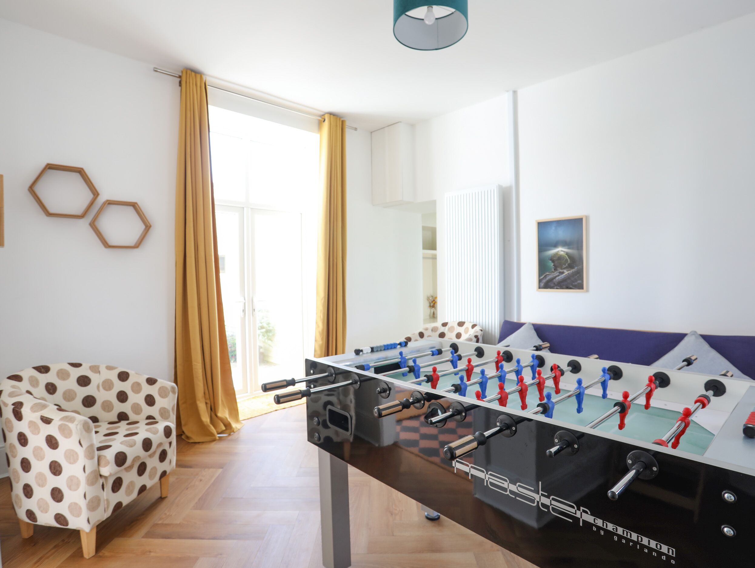 A room with a foosball table, a polka dot chair, and a view through a large window.