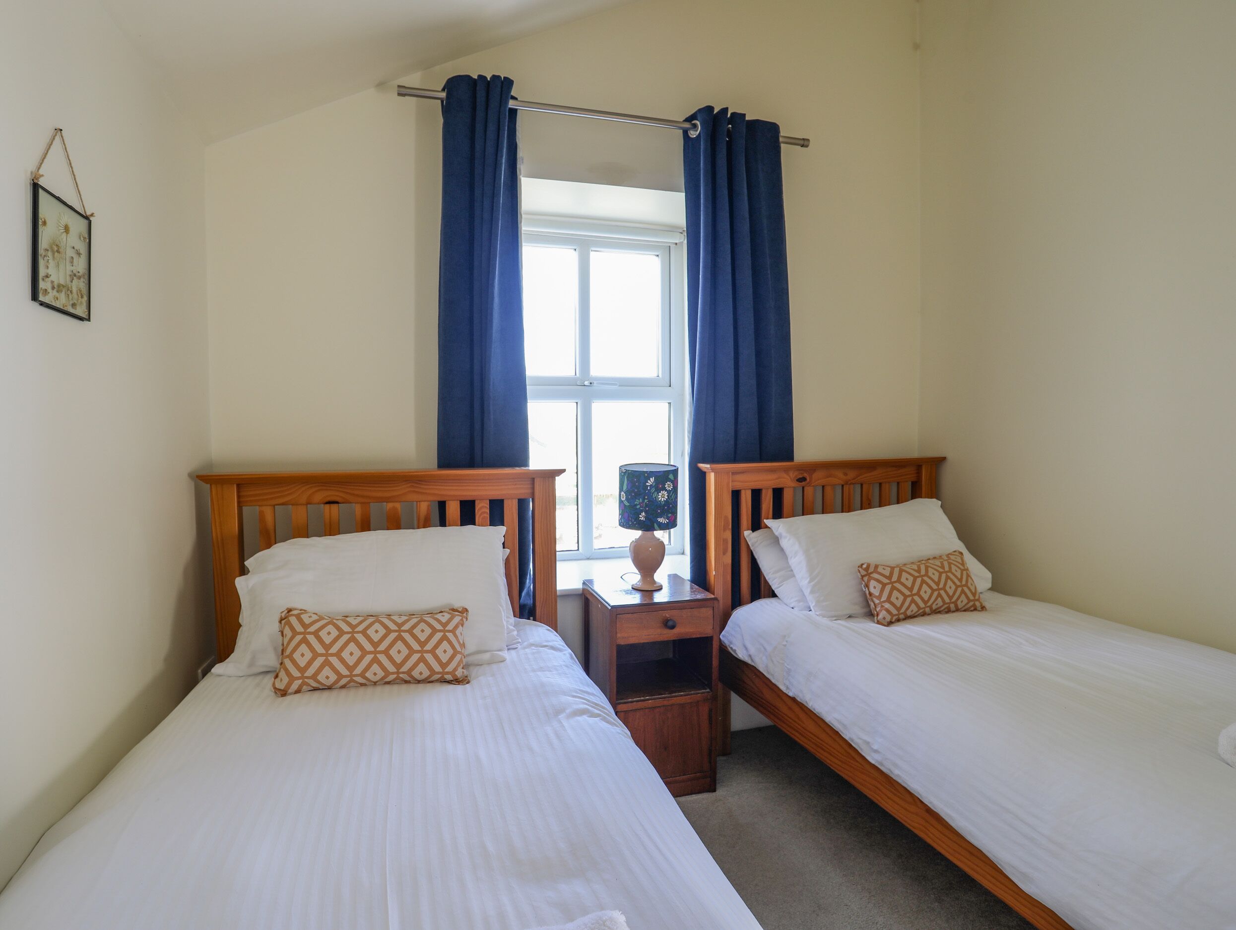 A room with two wooden beds, white bedding, and blue curtains.